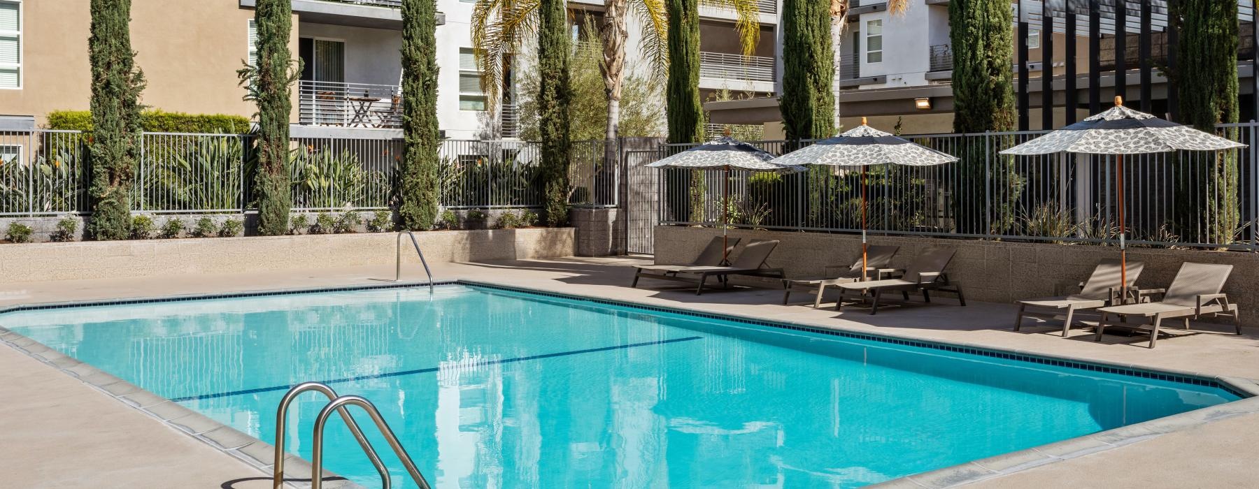 a pool with chairs and umbrellas by a building